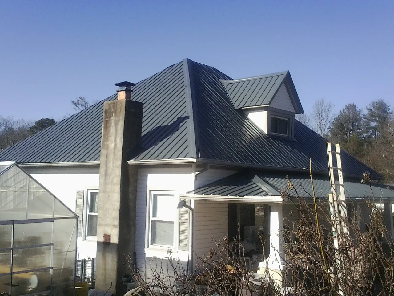 Dark blue standing seam metal roof on a white farmhouse with dormer — Slate & Tile Roof Repair by Roofing Brothers in Garden Grove