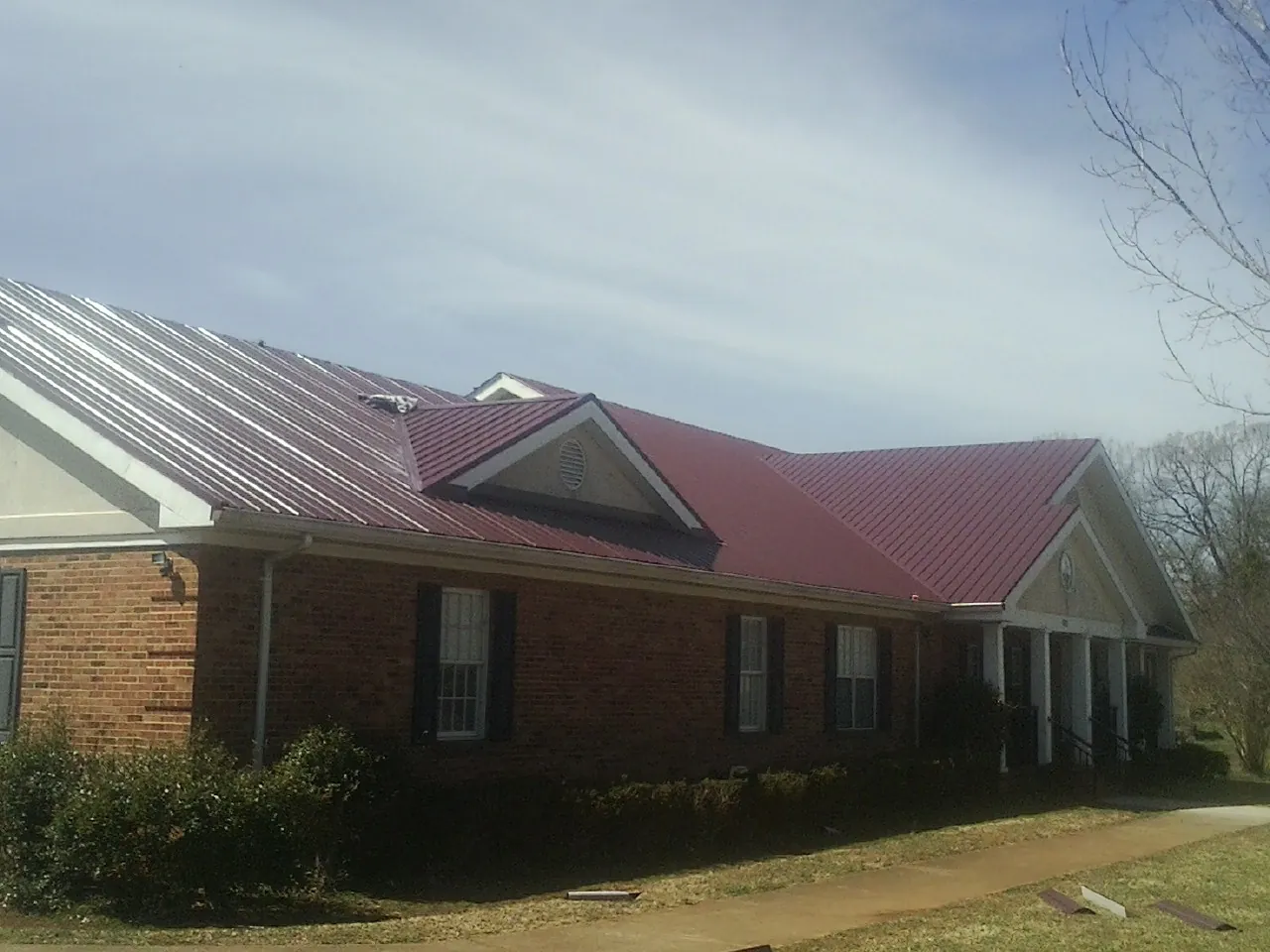 Red metal roof with gabled entries on a long brick building, from a Hail Damage Roof Repair job in Garden Grove